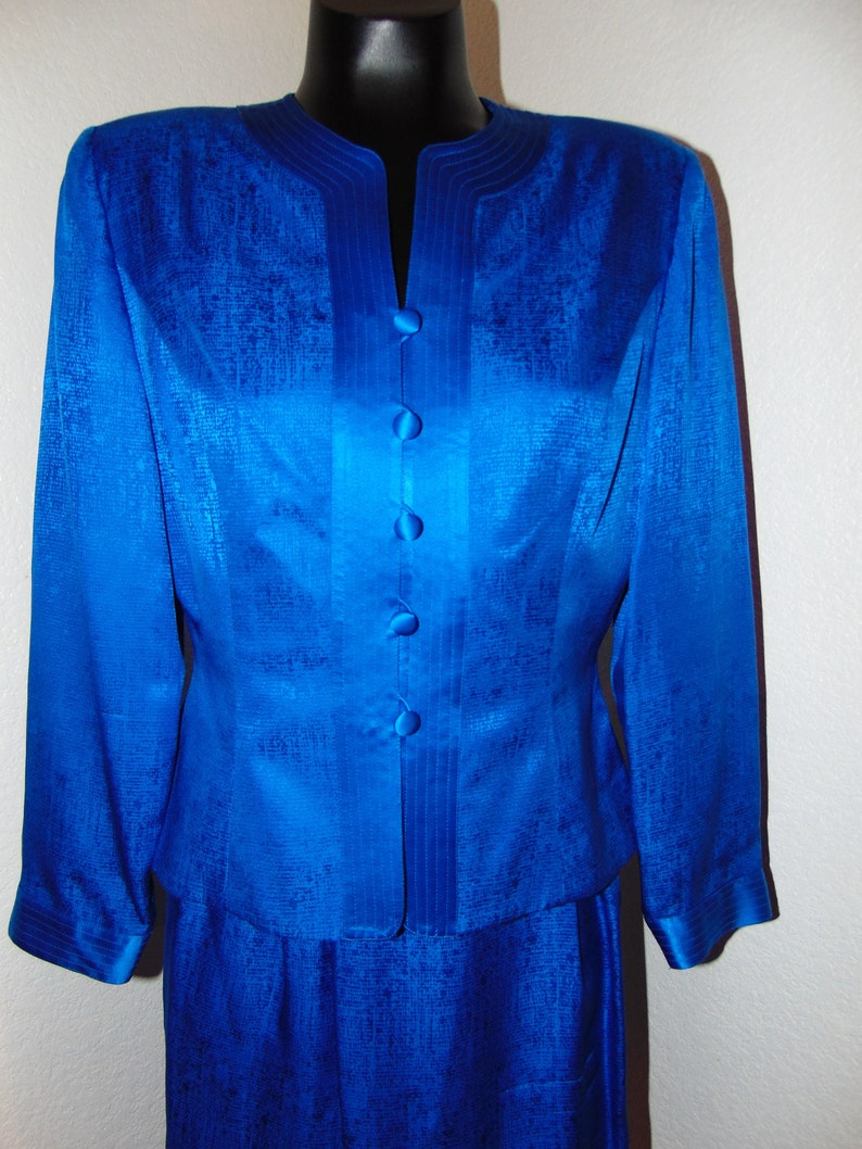 May include: A royal blue silk suit jacket and skirt with a satin finish and a row of buttons down the front.