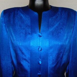 May include: A royal blue blazer with a satin finish and a V-neck collar. The blazer has a decorative trim around the collar and four buttons down the front.
