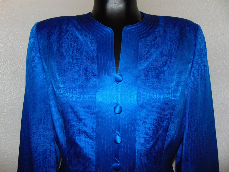 May include: A royal blue blazer with a satin finish and a V-neck collar. The blazer has a decorative trim around the collar and four buttons down the front.