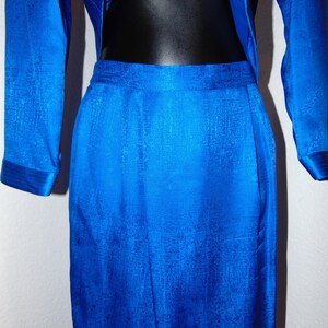 May include: A royal blue skirt suit with a textured fabric. The skirt is A-line and the jacket has long sleeves.