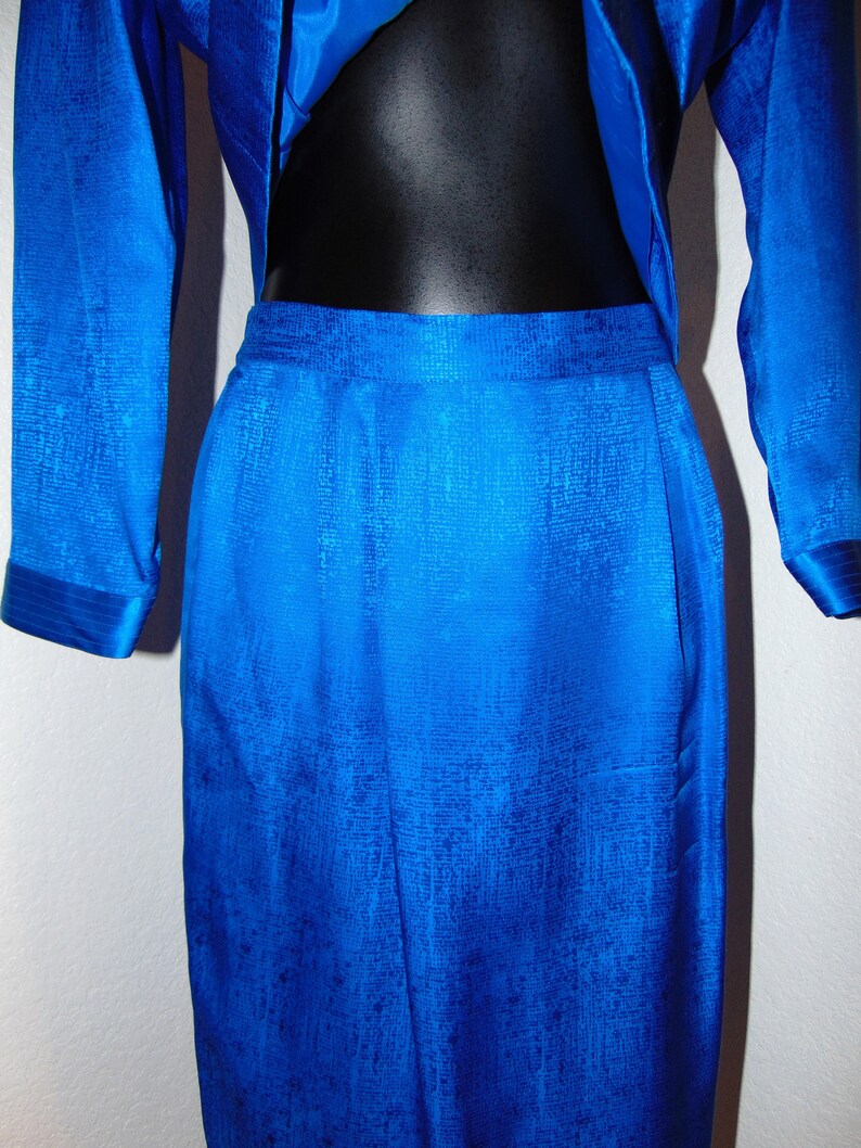 May include: A royal blue skirt suit with a textured fabric. The skirt is A-line and the jacket has long sleeves.