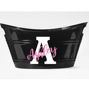 May include: Black metal tub with a curved top. A large white letter "A" is centered on the front, with the name "Ashley" in pink script overlaid on the letter. The tub has a simple, elegant design.