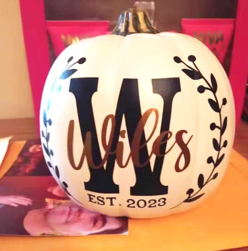 May include: A white pumpkin with a black letter "W" and the word "Wiles" in a cursive font. The pumpkin is decorated with a black floral design and the text "EST. 2023".