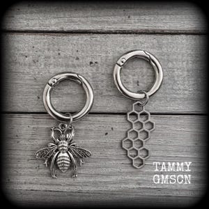 May include: Two silver keychains with charms. One keychain has a silver bee charm and the other has a honeycomb charm. The keychains are on a wooden background.