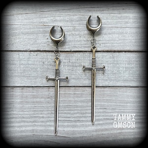 May include: A pair of silver sword earrings with a crescent moon design. The swords have a gold accent on the hilt.