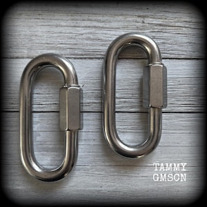 May include: Two stainless steel oval quick links with a hex nut closure. The links are shown against a weathered, gray wooden background. The text "TAMMY GMSCN" is visible in the lower right corner.