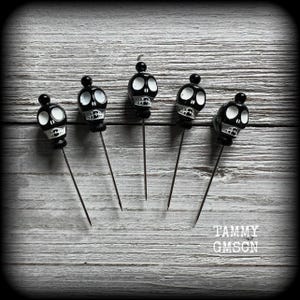 May include: Five black skull-shaped cocktail picks with white detailing, displayed on a weathered, grey wooden surface. Each pick has a small, round black top. The text "TAMMY GMSON" is visible in the lower right corner.