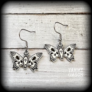 May include: A pair of silver butterfly earrings with black and white details. Each butterfly has a skull design and a small coffin with a cross on it.