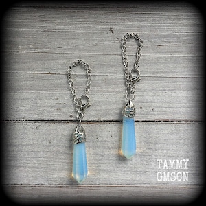 May include: Two silver chains with opal teardrop pendants. The chains have a clasp closure. The teardrops are a light blue colour.