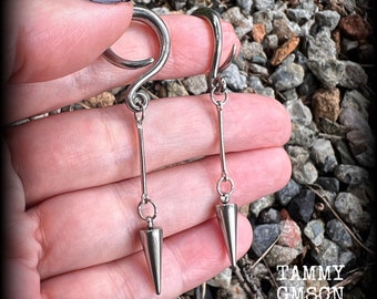 May include: A pair of silver-toned metal ear gauges featuring a spiral-shaped top section. Each gauge has a thin vertical bar dangling from the spiral, which connects to a pointed, cone-shaped charm at the bottom. The jewelry has a polished finish.