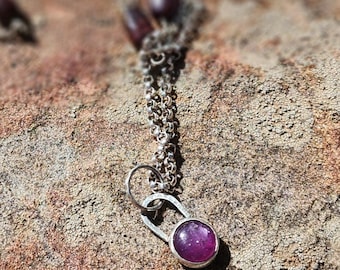 May include: A silver chain necklace with a pendant featuring a round, purple gemstone set in a silver bezel.