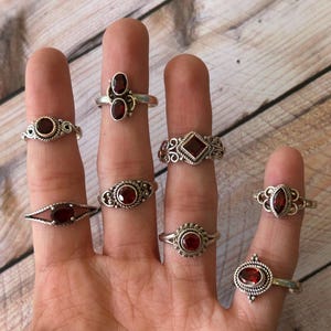 May include: Eight silver rings with red gemstone settings. The rings feature various designs, including a ring with two gemstones, a ring with a square gemstone, and a ring with a round gemstone.