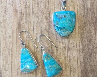May include: A set of turquoise and sterling silver earrings and a pendant necklace. The turquoise stones are a vibrant blue with brown and white marbling. The earrings are dangle style with a teardrop shape. The pendant is a teardrop shape with a silver bail.