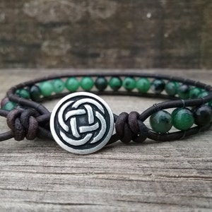 May include: A brown leather bracelet with green gemstone beads and a silver Celtic knot charm.
