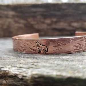 May include: A copper bracelet with a hammered texture and a wolf silhouette design.