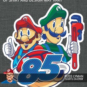 May include: A sticker featuring cartoon characters Mario and Luigi, with a red and blue design, thumbs up, and a red wrench. The text reads "Since '85" and "Russ Lyman Shirts on Etsy". The artist's mock-up may vary.