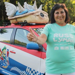 May include: A red, white, and blue car with a large Bowser shell on top. The car features Mario and Luigi graphics and the number 85. The person is wearing a light green t-shirt with the text "RUSS LYMAN".