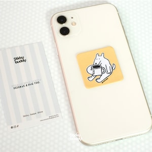 Op de afbeelding: Een witte smartphone met een vierkante gele sticker met een witte hond die een mok vasthoudt. Daarnaast ligt een rechthoekige kaart met lichtgrijze strepen, de tekst Sticky buddy, BECAUSE YOUR SCREEN DESERVE A HUG TOO, en Sticky . Swipe . Shine.