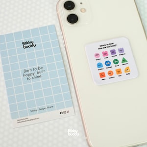 Op de afbeelding: Een witte smartphone met een vierkante sticker met een raster van twaalf kleurrijke emotiepictogrammen en de tekst Check-in time: How are you today? Daarnaast ligt een lichtblauwe kaart met een ruitjespatroon en de tekst Sticky buddy Born to be happy, built to shine.