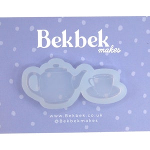 May include: A light blue silicone mould featuring a teapot and teacup design. The mould is on a light purple card with white polka dots. The text "Bekbek makes" and website details are visible.