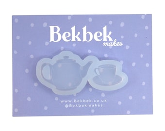 May include: A light blue silicone mold featuring a teapot and teacup design. The mold is on a light purple card with white polka dots. The text "Bekbek makes" and website information are visible.