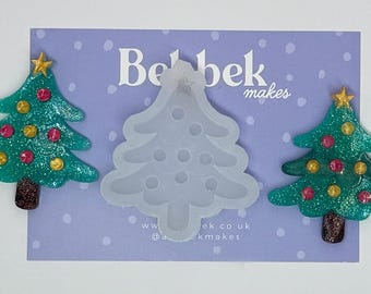 May include: The image shows two teal glitter Christmas tree decorations with gold and red baubles and a gold star on top. A clear silicone Christmas tree mould is in the centre. The background is a lilac card.