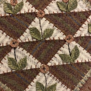 May include: A handcrafted, quilted textile featuring a repeating geometric pattern. The design incorporates brown, green, and cream-colored fabrics, with embroidered floral accents. The piece is likely a decorative item, such as a placemat or coaster.