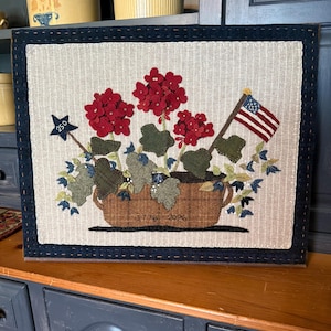 May include: A framed textile art piece featuring a floral arrangement with red flowers, green leaves, and an American flag. The artwork includes a star with the number 250 and the dates 1776-2026.