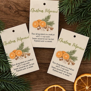 Puede incluir: Tres etiquetas color crema con el texto "Christmas Potpourri" e ilustraciones de naranjas, palitos de canela y ramitas de pino. Rodajas de naranja secas y ramas de pino están esparcidas alrededor de las etiquetas.