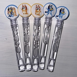 May include: Six clear plastic bubble wands with colorful character stickers featuring a blue dog with a red collar and a brown dog with a yellow collar. The stickers are round and have white backgrounds.