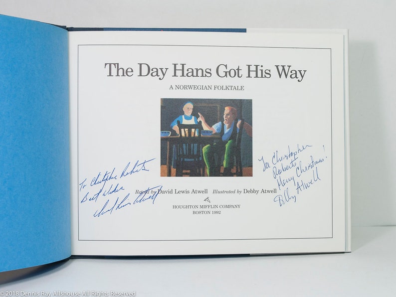 May include: Open book with the title "The Day Hans Got His Way" and a Norwegian folktale. The illustration shows two people at a table. The book has blue covers and handwritten signatures.