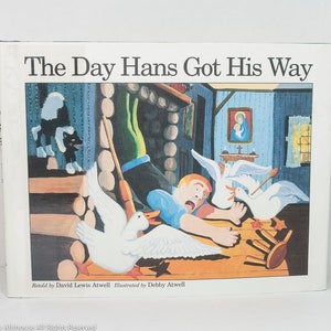 May include: A children's book titled "The Day Hans Got His Way" with a colorful illustration. The cover art depicts a chaotic scene with a frightened boy, geese, and a skunk. The book is retold by David Lewis Atwell and illustrated by Debby Atwell.