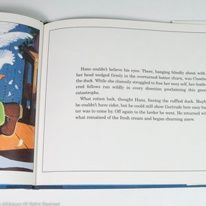 May include: An open book with a colorful illustration and text. The illustration depicts a white swan, green objects, and a wooden floor. The text describes a duck stuck in a butter churn and the events that follow.