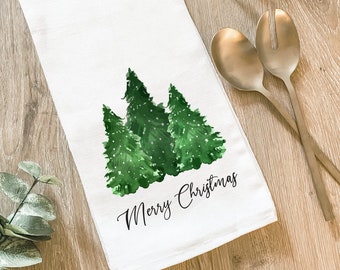 Peut inclure: Serviette de cuisine blanche avec une illustration aquarelle de trois sapins de Noël verts et le texte "Joyeux Noël".