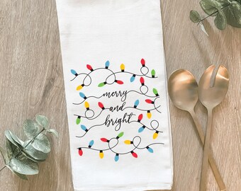 Peut inclure: Serviette de cuisine blanche avec un motif de lumières de Noël colorées et le texte "merry and bright".
