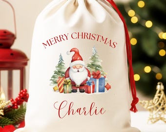 May include: A cream-colored Christmas gift bag with a red drawstring. The bag features a watercolor illustration of Santa Claus, Christmas trees, and wrapped presents. The words "MERRY CHRISTMAS" and the name "Charlie" are printed in red.