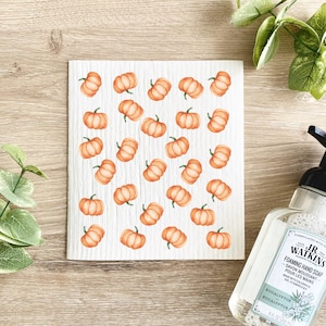 May include: White kitchen sponge with a repeating pattern of orange pumpkins. The sponge is made of cellulose and is designed for cleaning dishes and other surfaces.