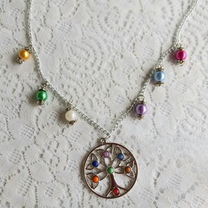 Puede incluir: Un collar de plata con un colgante de árbol de la vida con piedras de colores. El collar tiene varias cuentas de varios colores, incluyendo verde, amarillo, azul y morado.