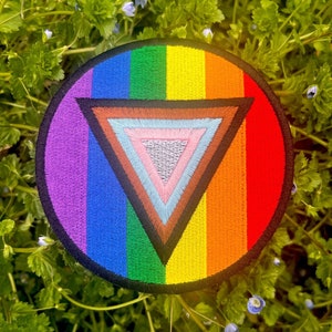 May include: A rainbow-colored embroidered patch with a black triangle in the center. The triangle is filled with smaller triangles in shades of brown, pink, blue, and gray.
