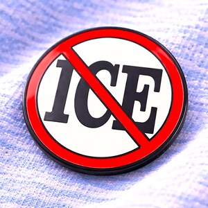 Może przedstawiać: Okrągła przypinka z białym środkiem, z napisem "ICE" pogrubioną czcionką w kolorze czarnym, przekreślonym czerwoną przekątną. Przypinka ma czerwoną obwódkę i czarną krawędź. Przypinka jest na jasnoniebieskim, teksturowanym tle.