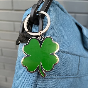 May include: A silver key chain with a green four-leaf clover charm attached to a blue bag.