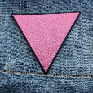 Puede incluir: Parche triangular rosa con contorno negro, cosido sobre una tela vaquera azul.