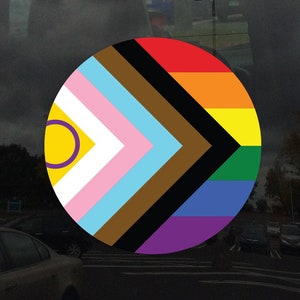 Puede incluir: Una pegatina circular con un diseño de bandera arcoíris. La bandera es una combinación de la bandera del orgullo transgénero, la bandera del orgullo intersexual y la bandera del orgullo progresista. La pegatina es perfecta para mostrar tu apoyo a la comunidad LGBTQ+.