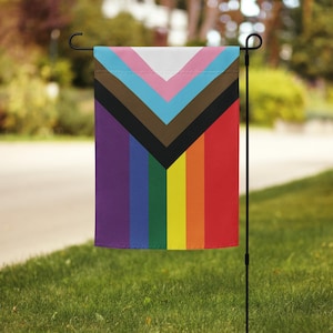 May include: A garden flag with a rainbow pride flag design. The flag features a purple, blue, green, yellow, orange, and red stripe pattern. The flag also has a black, brown, light blue, and pink chevron pattern.
