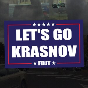 May include: A blue and red political campaign sign with white text that reads "LET'S GO KRASNOV" and "FDJT" in stars.