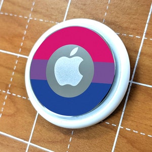 Może przedstawiać: Okrągły biały dodatek do telefonu z srebrnym logo Apple na niebieskim, fioletowym i różowym tle.
