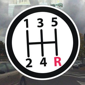 Può includere: Un adesivo circolare bianco con bordo nero raffigurante uno schema del cambio. I numeri 1, 2, 3, 4 e 5 sono visualizzati, insieme alla lettera "R" in rosso, che indica la retromarcia.