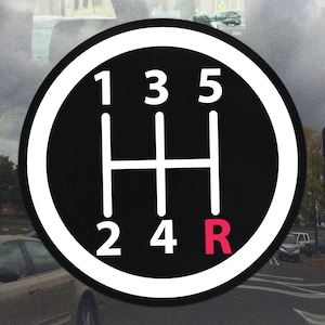Può includere: Adesivo in bianco e nero con il cambio marce di un'auto. I numeri 1, 2, 3, 4, 5 e R sono bianchi, la R è rossa. L'adesivo è circolare con un bordo bianco.