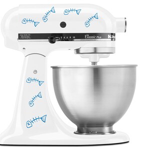 Puede incluir: Batidora de pie blanca con un tazón plateado y calcomanías azules de espinas de pescado. La batidora tiene un panel de control con el texto "Classic Plus" y "KitchenAid".
