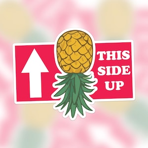 Op de afbeelding: Een rode en witte sticker met een pijl die omhoog wijst en de tekst "THIS SIDE UP" met een ananasillustratie.